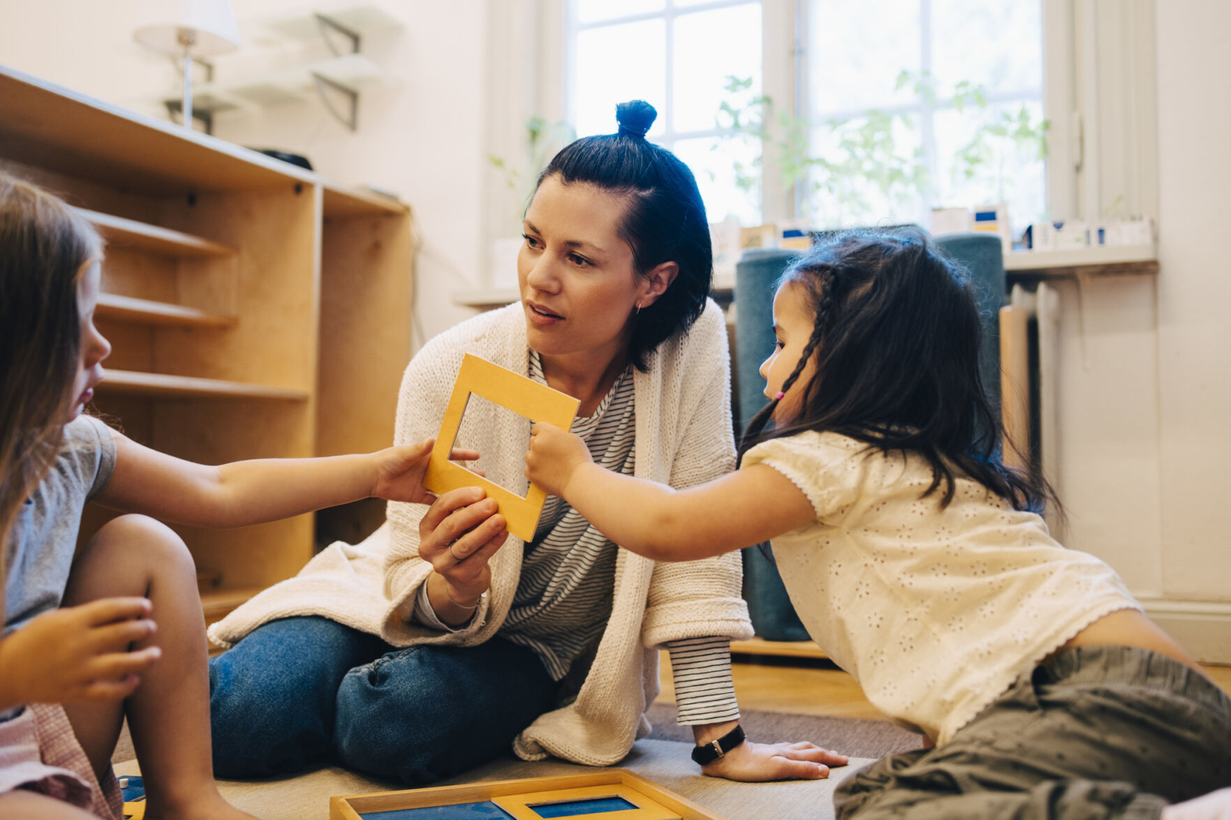 Female teacher and students holding picture frame while sitting in classroom at child care (copy)
